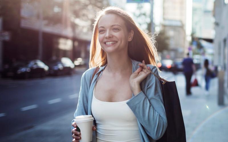 a woman holding a coffee cup walks down the street
